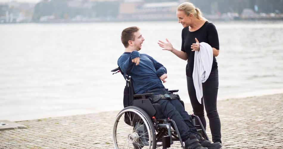 A man in wheelchair and his carer outside next to the river.