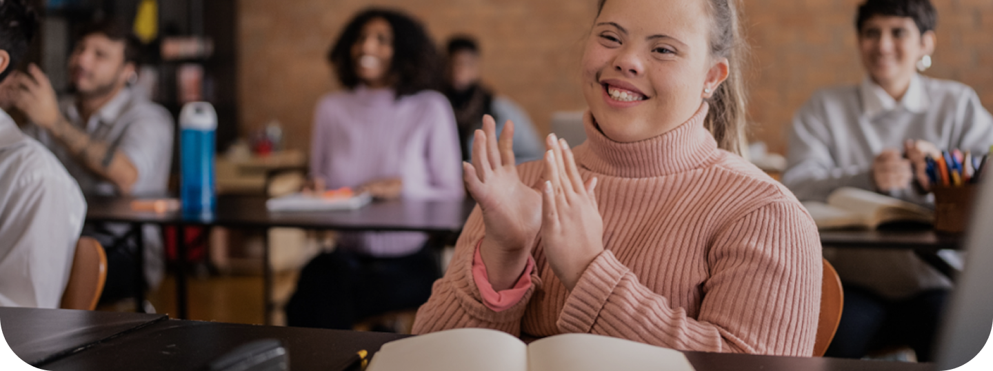 A young girl in a classroom clapping her hands and smiling.