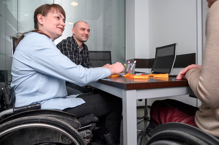 A woman in a wheelchair and her two colleagues sitting at a conference desk in an office environment having a meeting.