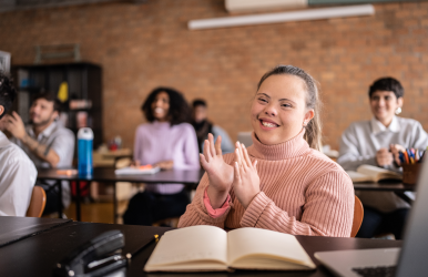 a young woman with a disability clapping and smiling in a classroom environment.