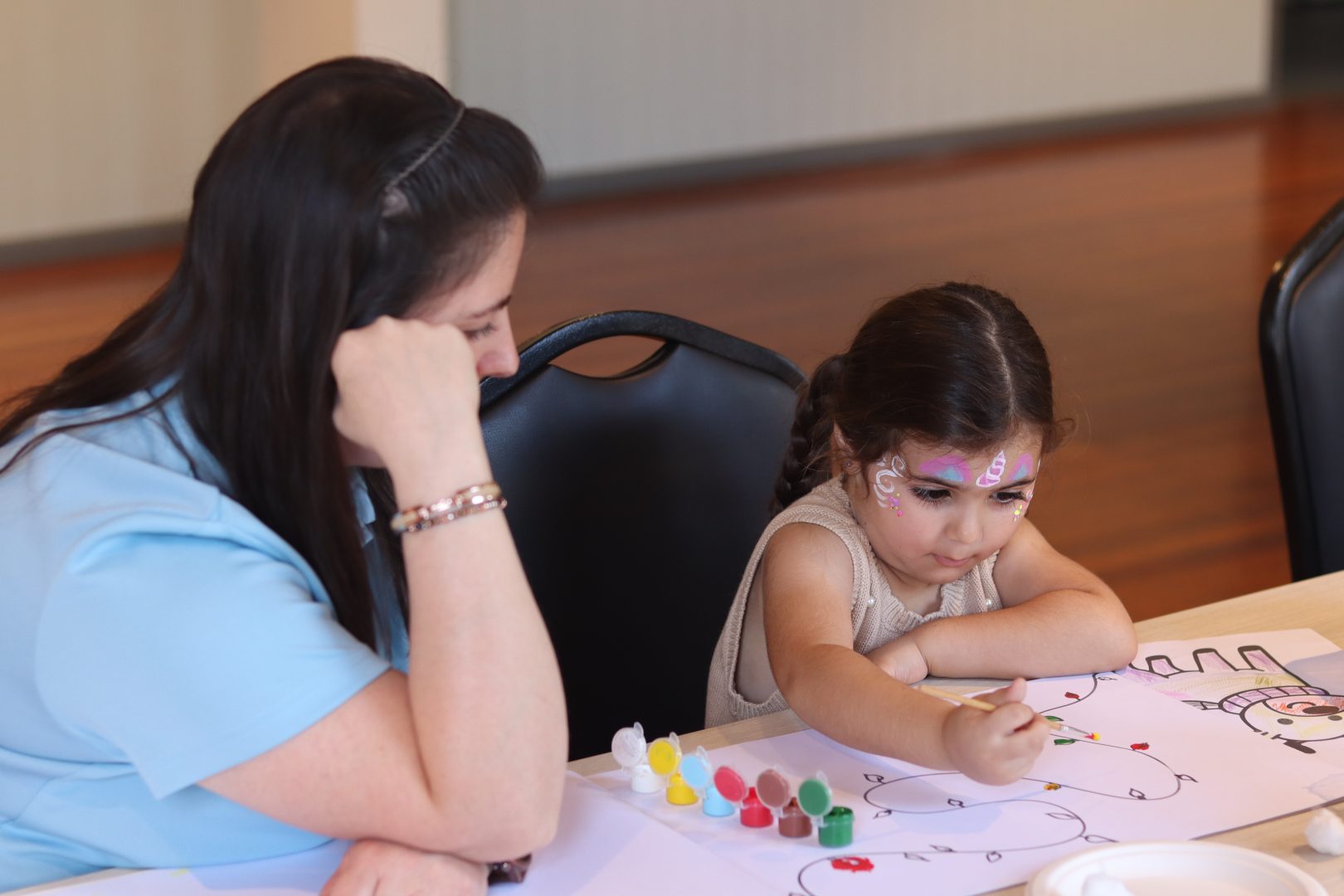A young girl is painting while a woman watches.